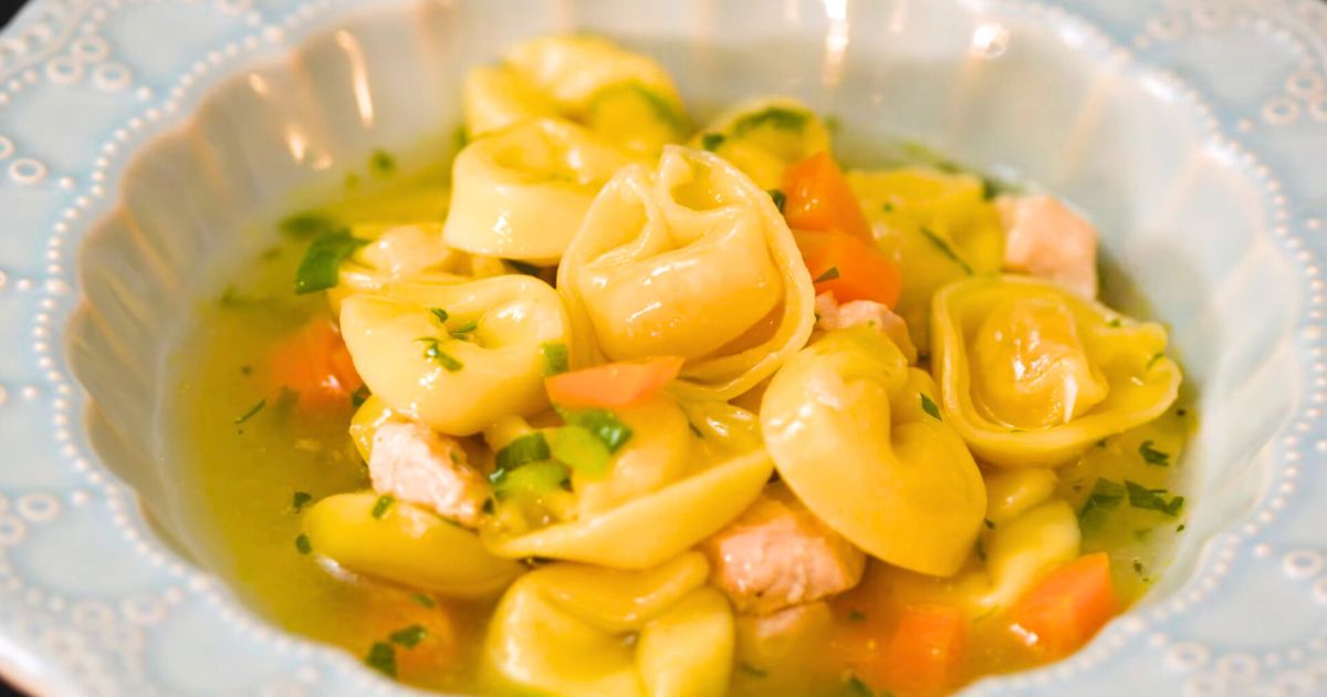 Sopa de capeletti quente em um prato fundo com ervas frescas.